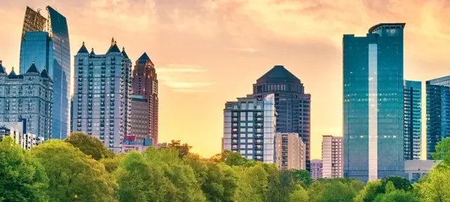 Panoramic view of the Atlanta skyline during sunset with modern skyscrapers and greenery in the foreground.