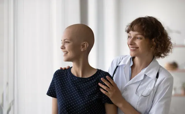 Smiling Caucasian doctor or nurse support comfort millennial woman struggle with oncology. Happy GP and optimistic female cancer patient look in distance dream of illness recovery or remission.